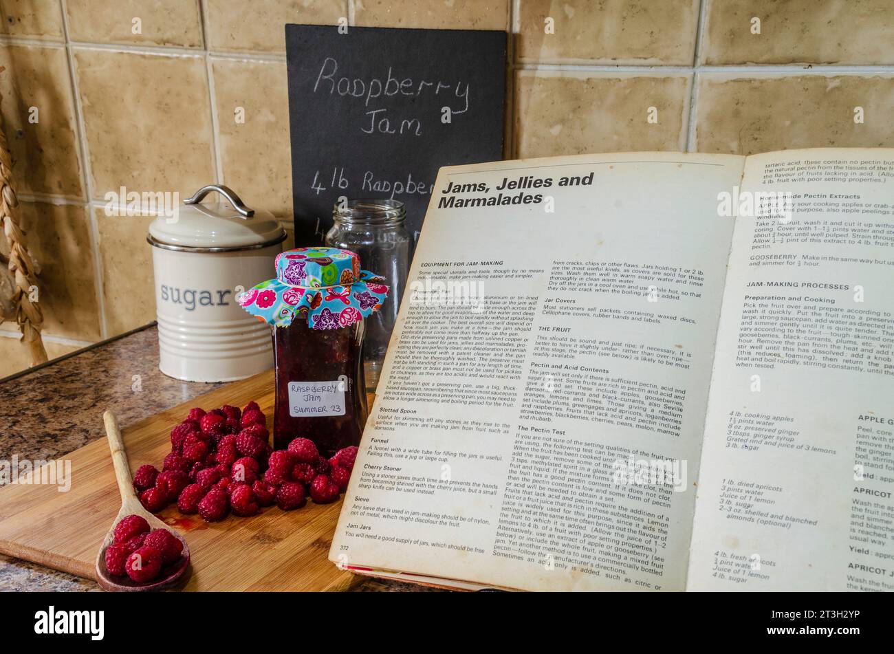 Lamponi e un barattolo di marmellata insieme a un ricettario su un piano di lavoro Foto Stock