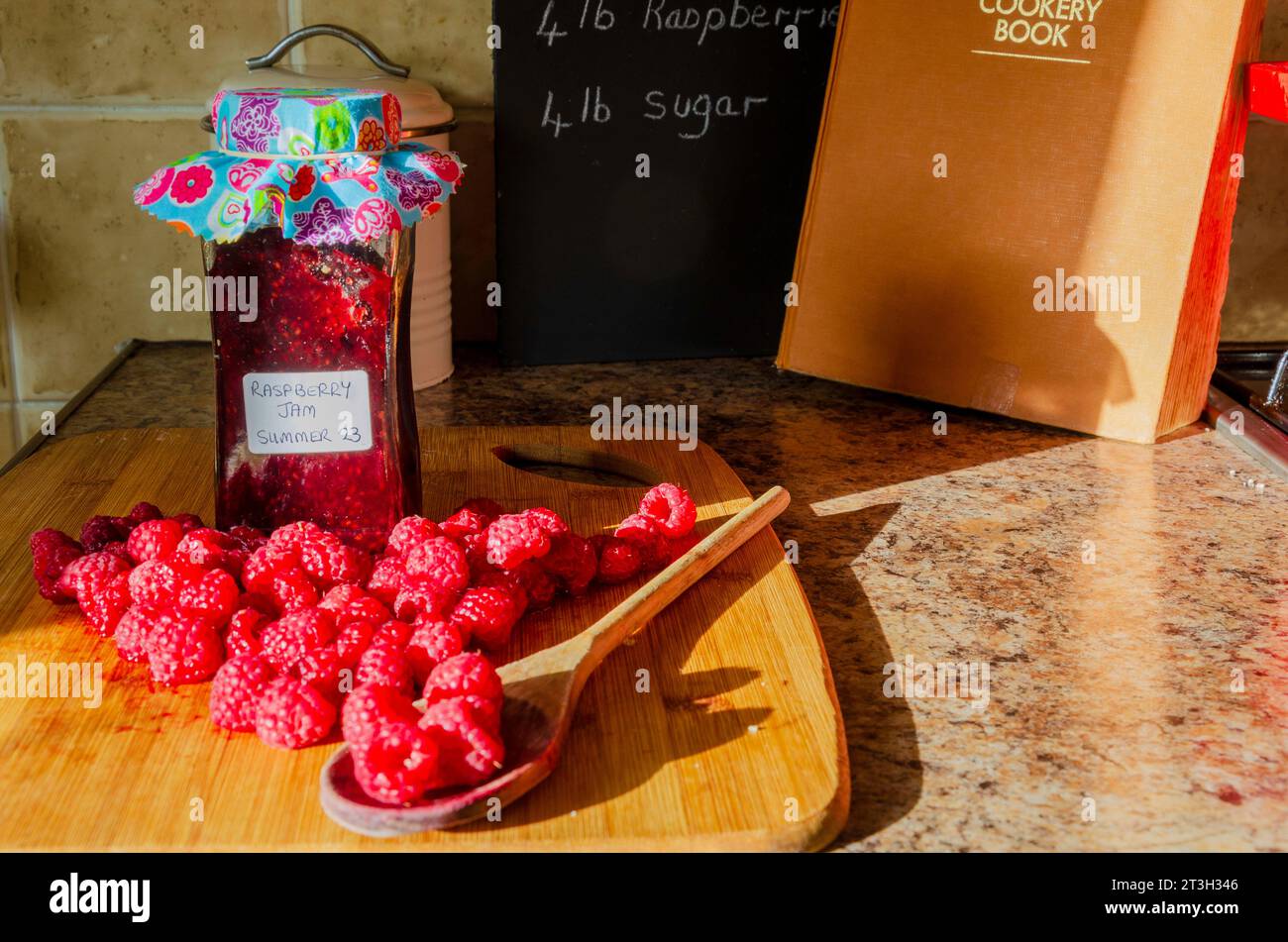 Lamponi, zucchero e un barattolo di marmellata insieme a un ricettario su un piano di lavoro Foto Stock