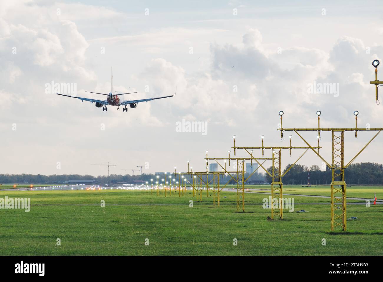 Un Boeing 737 vola sopra le luci di avvicinamento atterrando sulla pista Polderbaan dell'aeroporto Schiphol di Amsterdam in un soleggiato pomeriggio autunnale Foto Stock