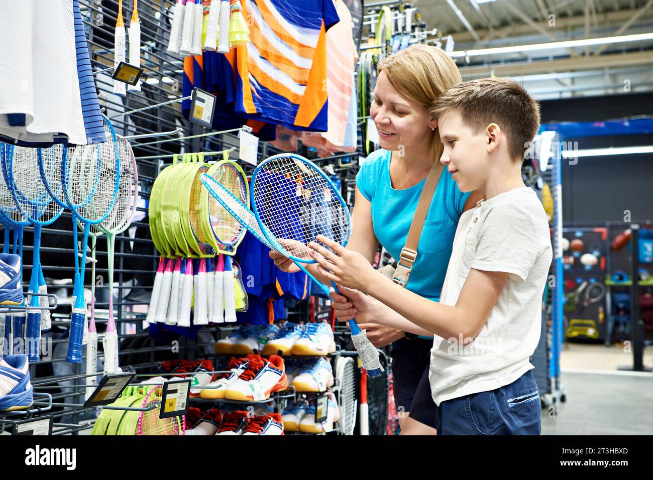 Il ragazzo con mamma sceglie le racchette da badminton in un negozio sportivo Foto Stock