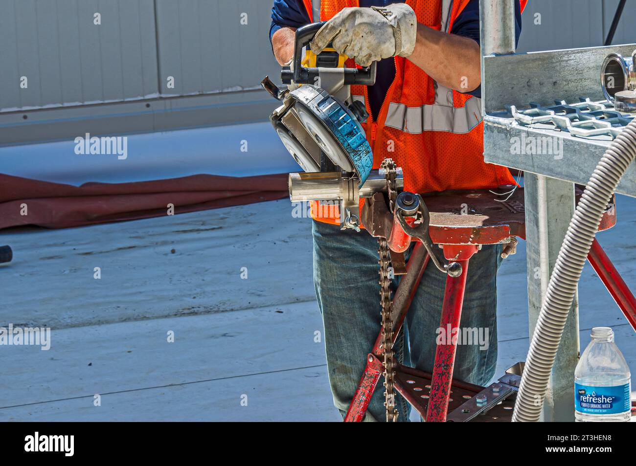 Un operaio edile utilizza una sega a nastro portatile per tagliare tubi in acciaio inox sul tetto di un impianto di refrigerazione industriale (stoccaggio a freddo). Foto Stock