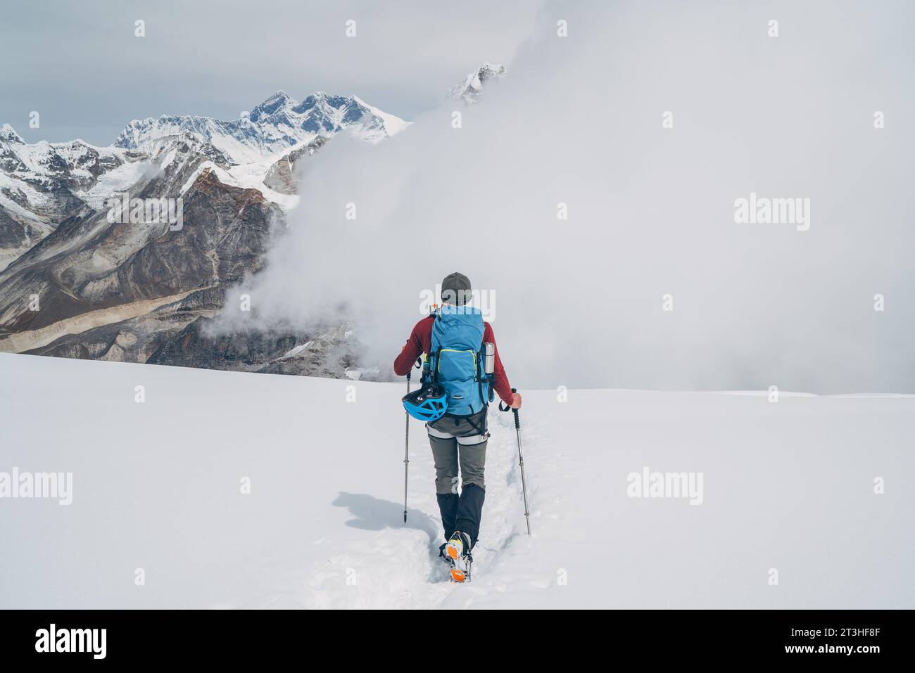 Arrampicatore con zaino e bastoni da trekking che scendono dalle alte pendici della vetta di Mera a 6000 metri di altitudine, ammirando il leggendario Monte Everest, Nuptse, Lhotse con South FAC Foto Stock