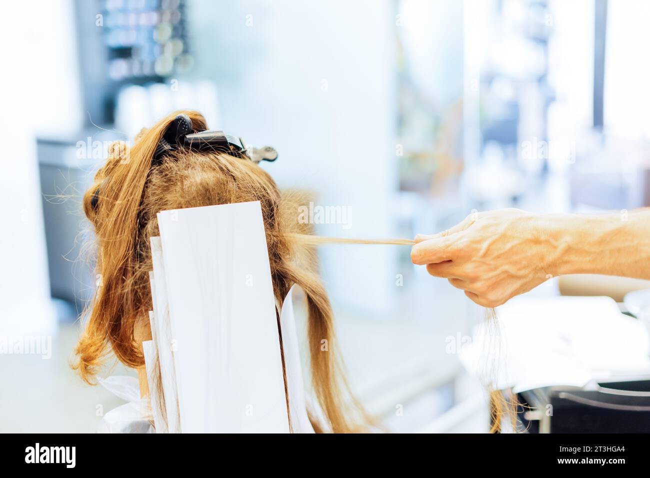 donna che ottiene luci, mano che tira un filo di capelli al parrucchiere Foto Stock