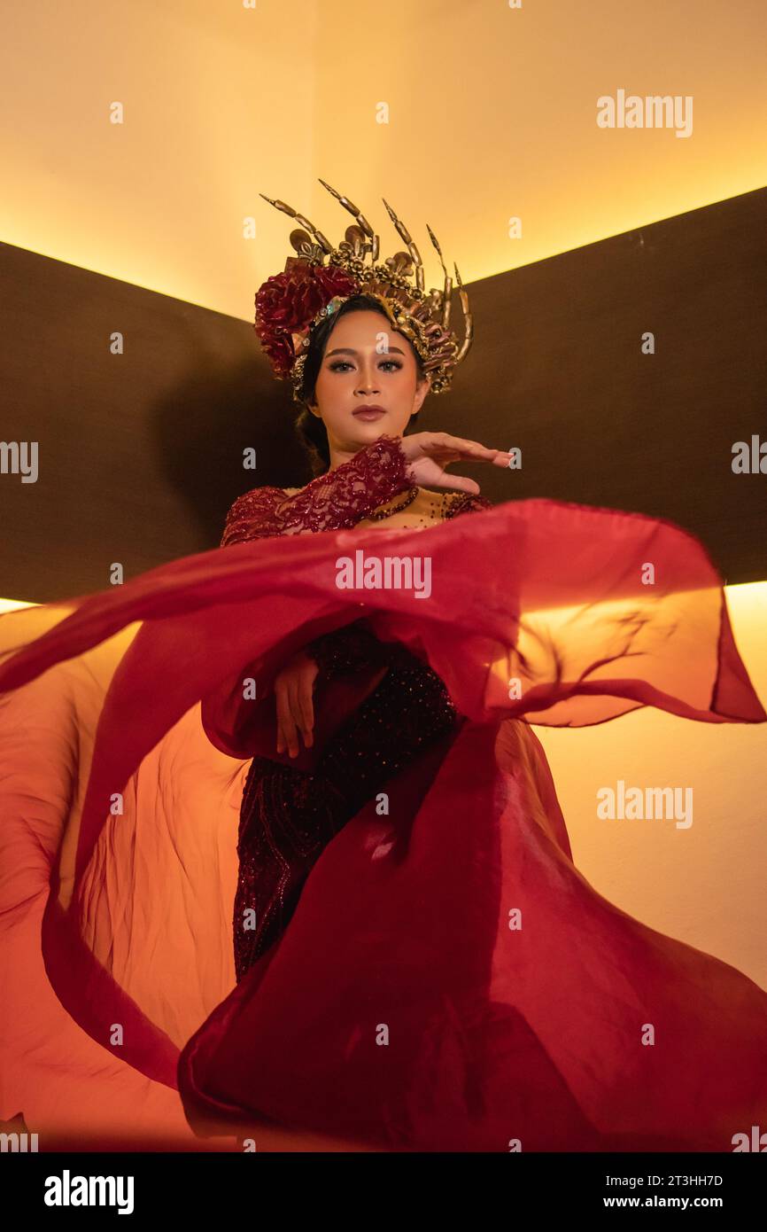 Una bella donna asiatica alza la coda di tessuto rosso indossando un abito da sposa rosso prima della cerimonia di nozze Foto Stock