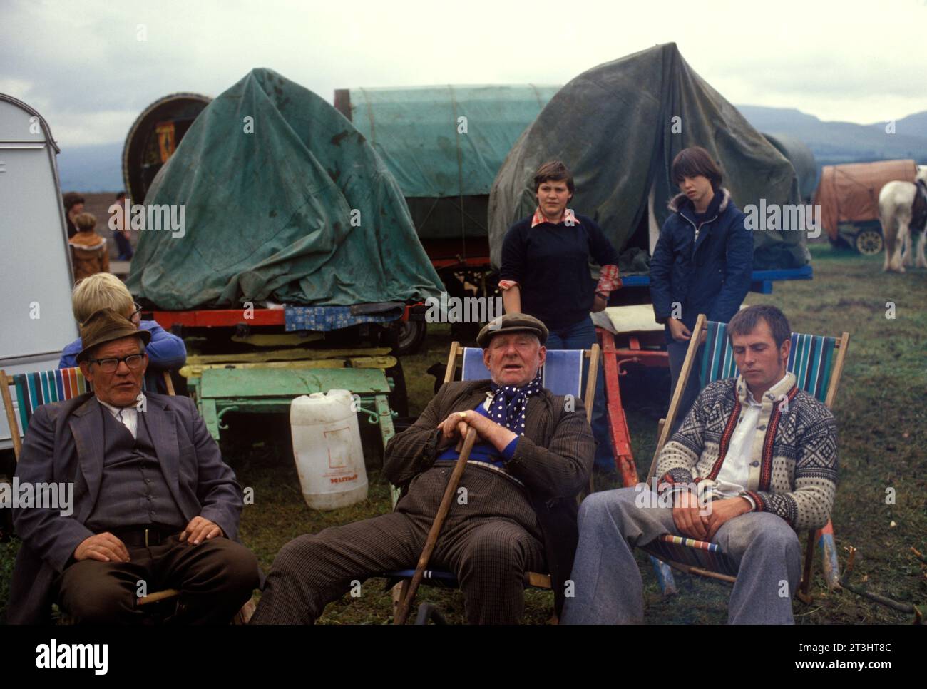 Gruppo di famiglia Gypsy, Appleby nel Westmorland, fiera dei cavalli gitani in Cumbria. Un gruppo di zingari siede intorno al fuoco del campo e passa l'ora del giorno. Le loro tradizionali roulotte in legno con tetto a prua sono sullo sfondo. Inghilterra Regno Unito giugno 1985 1980s UK Charter Fair concessa da re Giacomo II 1685 HOMER SYKES Foto Stock