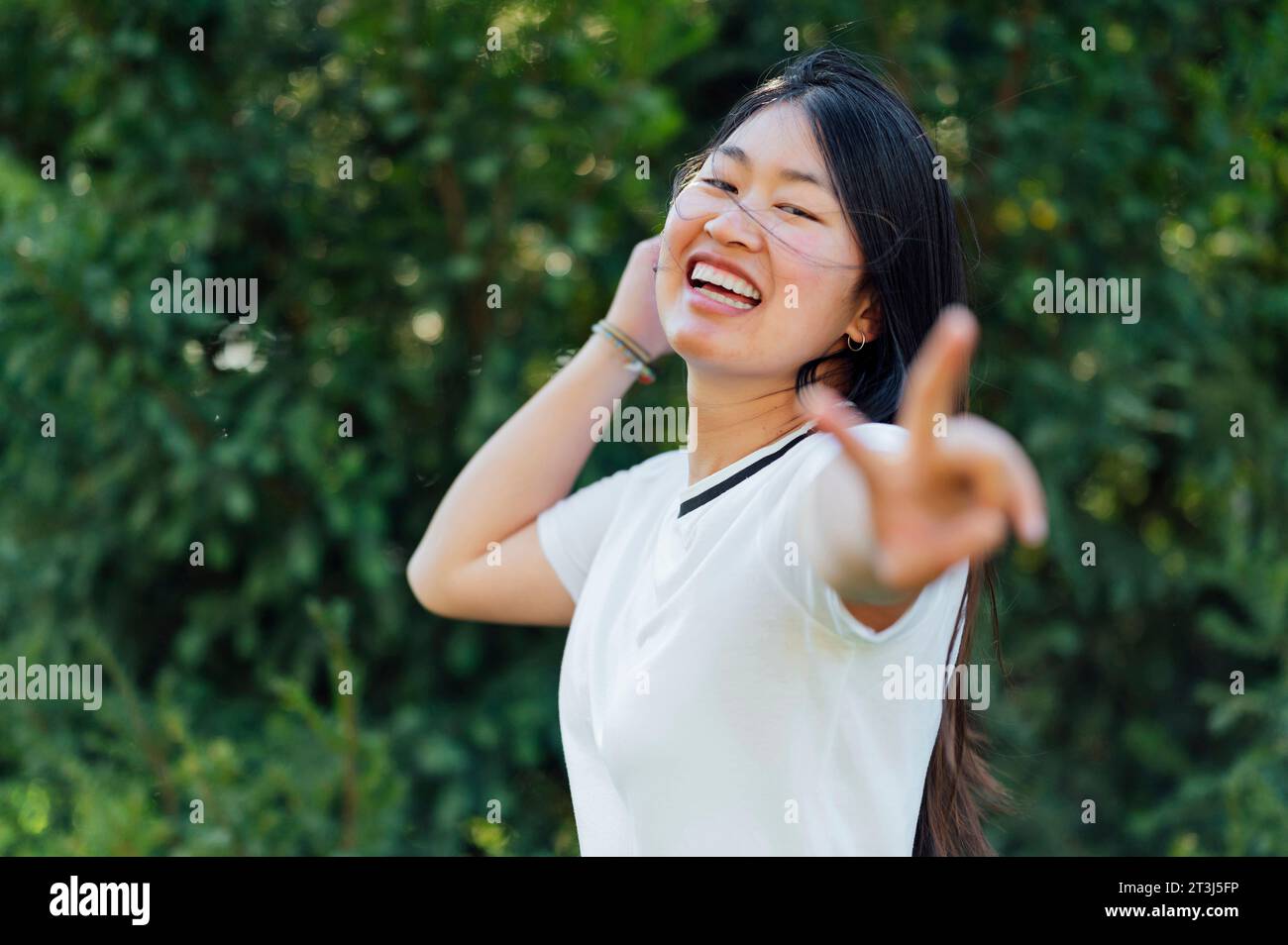 Giovane donna asiatica caucasica che fa il segno di pace all'aperto Foto Stock