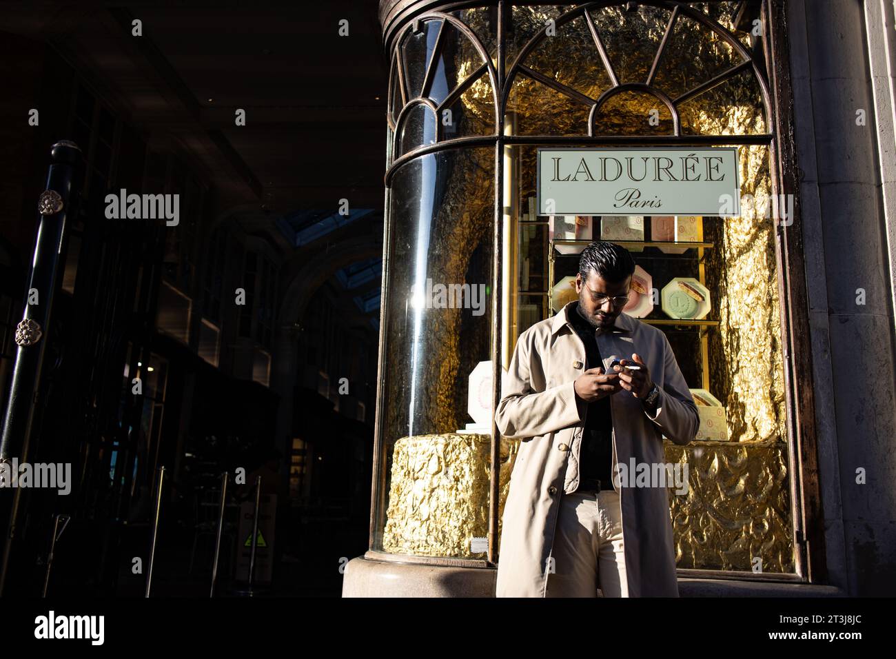 Uomo asiatico su smartphone all'esterno della pasticceria parigina LADURÉE, famosa per il suo macaron iconico, Burlington Arcade, Piccadilly, Londra, Regno Unito Foto Stock