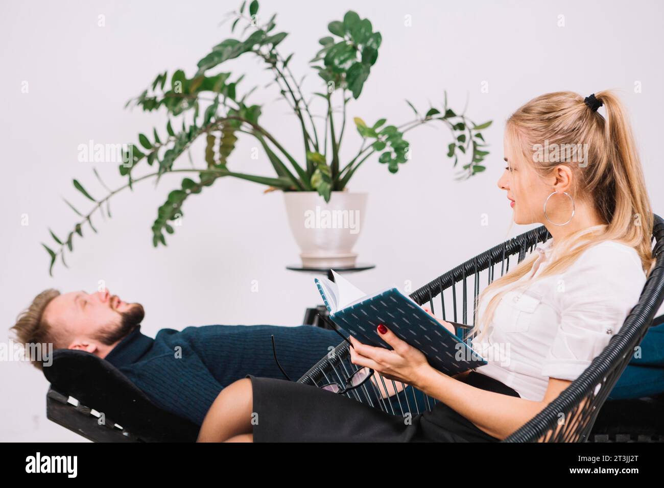 Bella psicologa femminile che sembra un paziente maschio sdraiato in una clinica sul divano Foto Stock