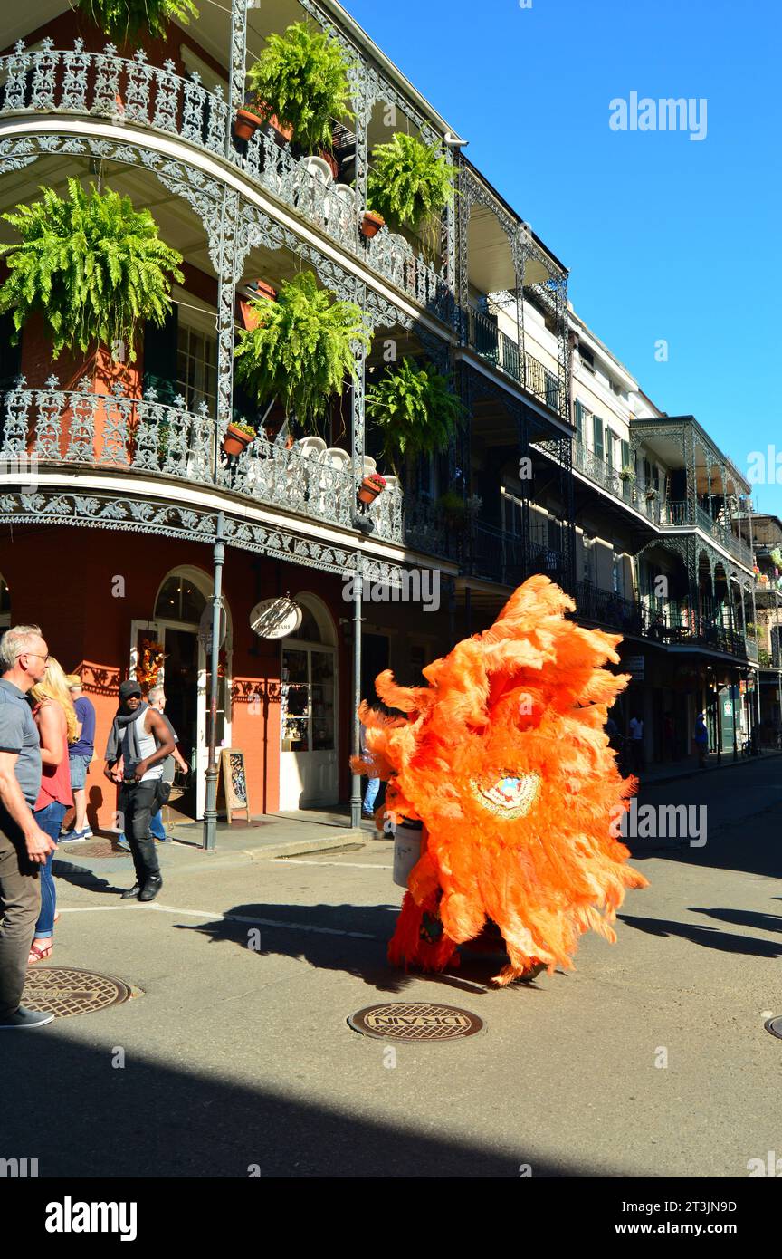 Un indiano del Mardi Gras, vestito con un elaborato costume arancione, cammina lungo gli edifici storici del quartiere francese di New Orleans Foto Stock