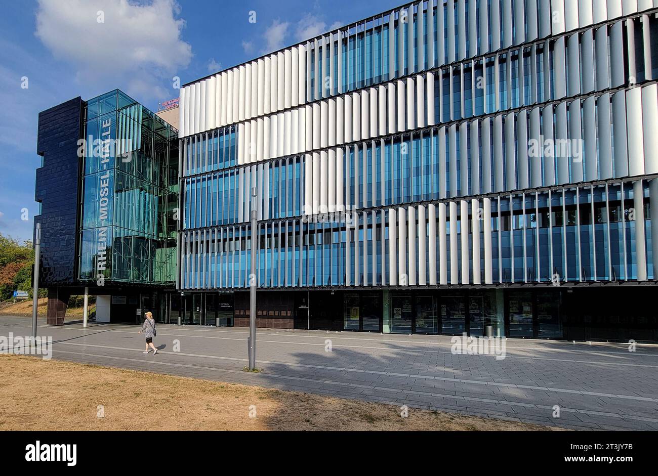Una donna solitaria cammina di fronte all'architettura moderna del Rhein-Mosel-Halle Business and Conference Center a Coblenza, Germania, vicino al fiume Reno. Foto Stock