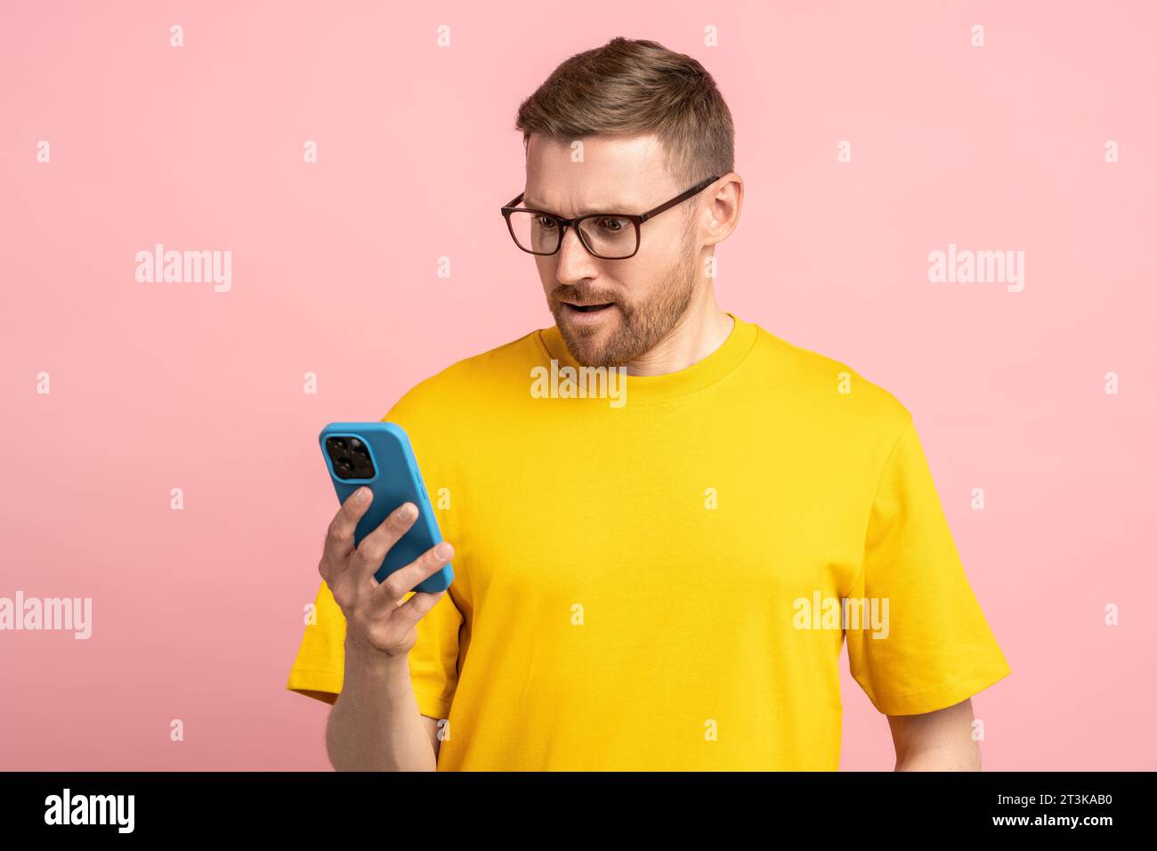 Un uomo barbuto con gli occhiali che guarda lo schermo del telefono cellulare con sorpresa scioccato dai messaggi e dalle notizie Foto Stock