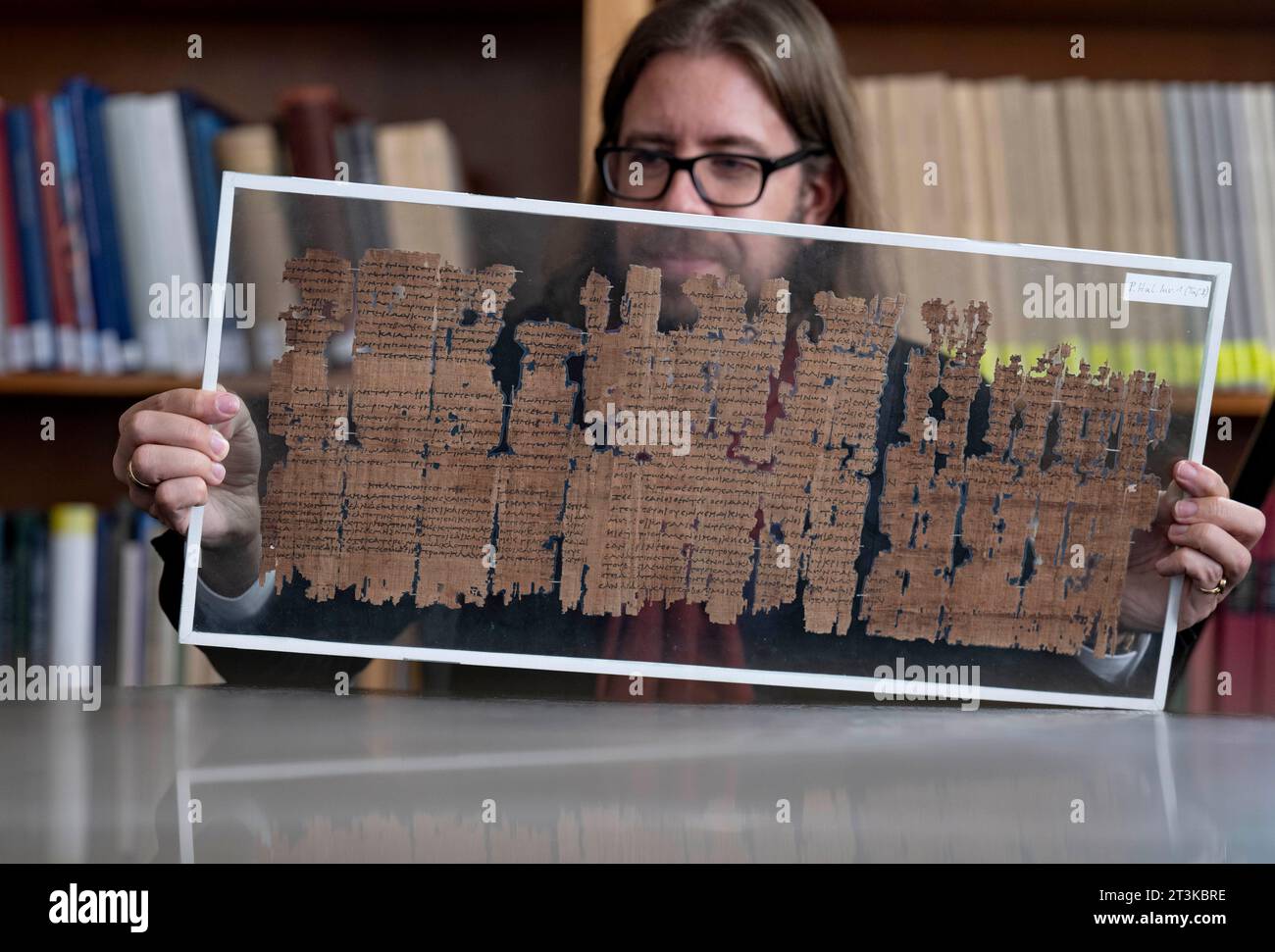 PRODUZIONE - 23 ottobre 2023, Sassonia-Anhalt, Halle (Saale): Una lastra di vetro con una preziosa lastra di papiro è tenuta nelle sue mani da Stefan Pfeiffer, storico e papirologo dell'Istituto di studi antichi dell'Università di Halle, nel museo archeologico dell'Università di Halle/Saale. Il foglio del III secolo a.C. contiene un estratto delle leggi della città di Alessandria. Con un progetto di ricerca su larga scala, le università di Colonia e Halle vogliono studiare l'antico stato dal 2024. (A dpa-Korr 'come funziona l'antico stato? - Gli scienziati esaminano i papiri di 2000 anni' Foto Stock