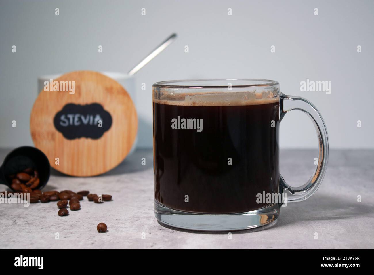 Un bicchiere di caffè nero e una ciotola con dolcificante stevia, sfondo grigio Foto Stock