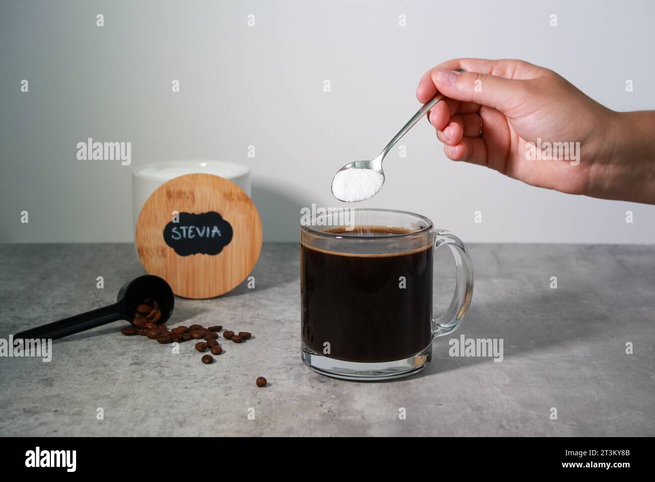 La mano della donna mette stevia dolcificante in un caffè nero, sfondo grigio Foto Stock