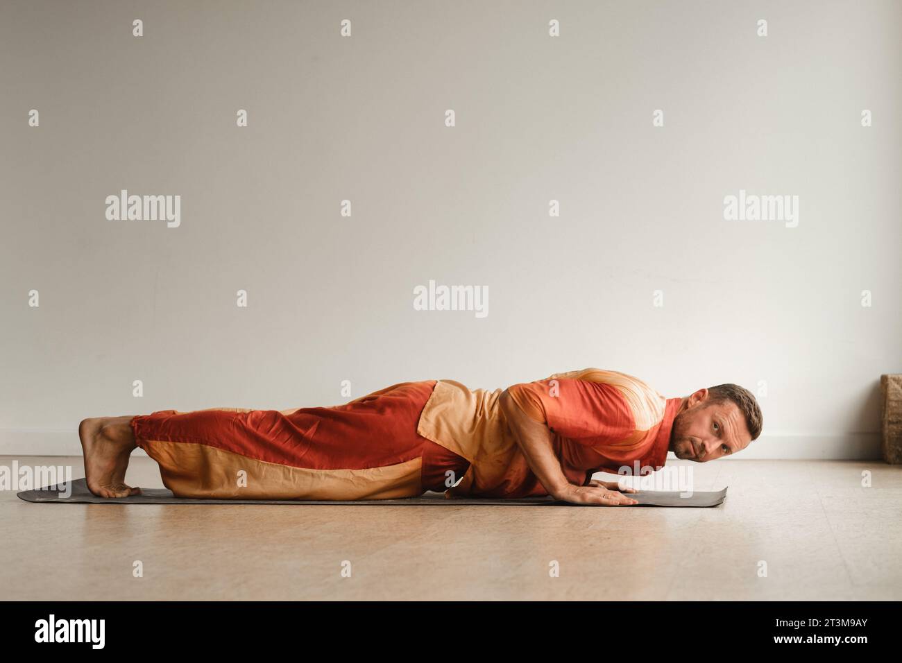 un uomo con una tuta arancione fa yoga in una sala fitness. Il concetto di salute. Foto Stock