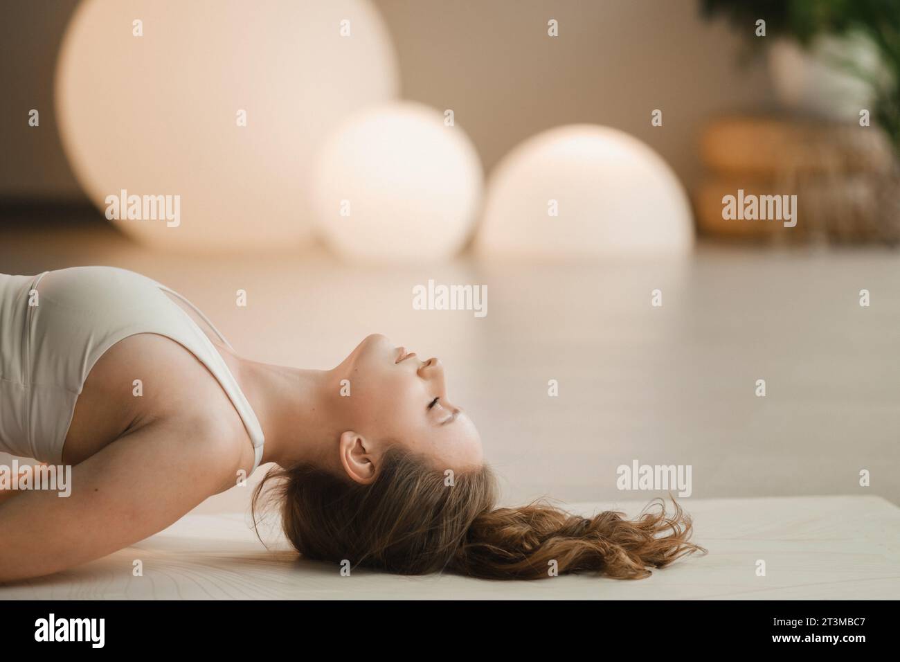 Una ragazza con vestiti bianchi fa yoga sdraiata su un tappeto al chiuso. Foto Stock