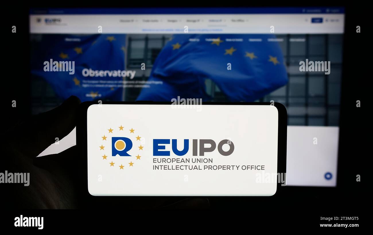 Persona che possiede uno smartphone con il logo dell'Ufficio dell'Unione europea per la proprietà intellettuale (EUIPO) davanti al sito web. Concentrarsi sul display del telefono. Foto Stock