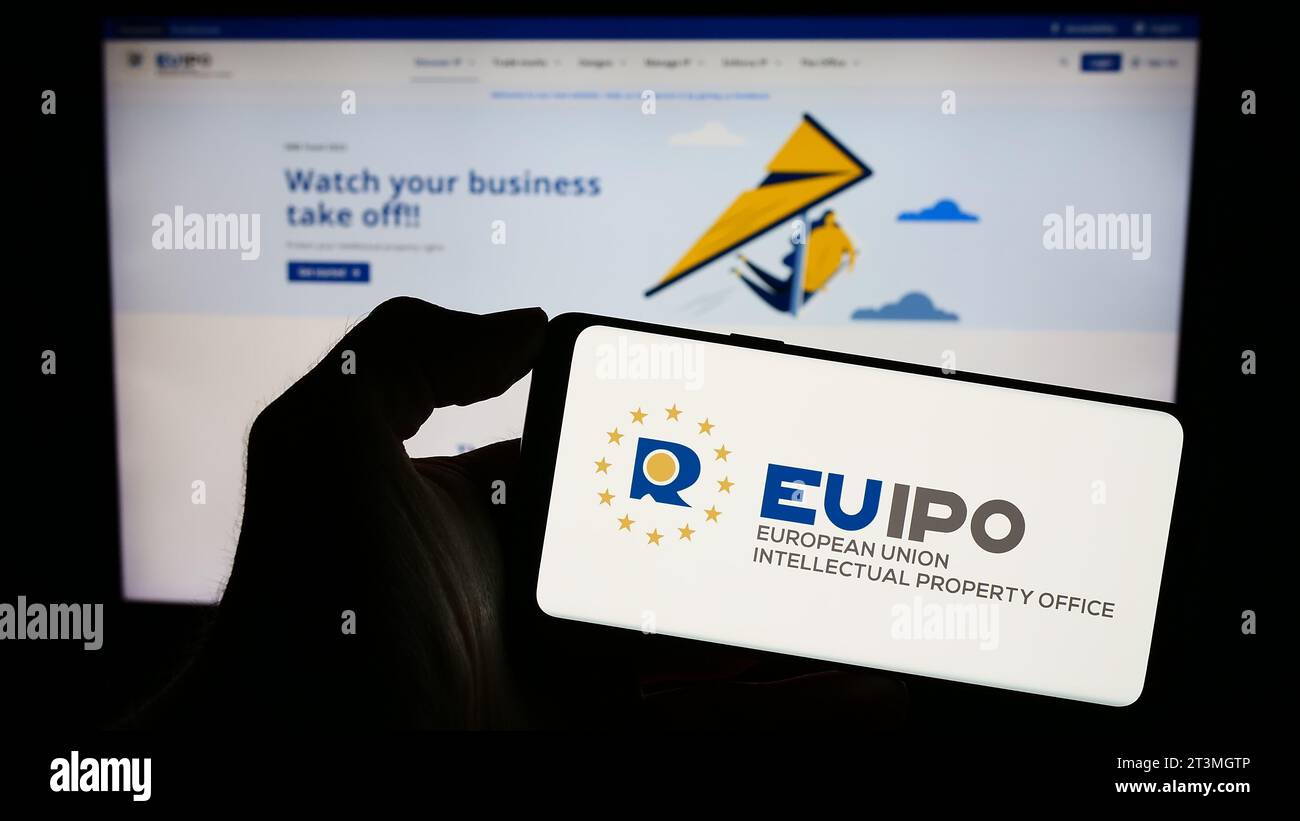 Persona in possesso di un cellulare con il logo dell'Ufficio dell'Unione europea per la proprietà intellettuale (EUIPO) davanti alla pagina web. Concentrarsi sul display del telefono. Foto Stock