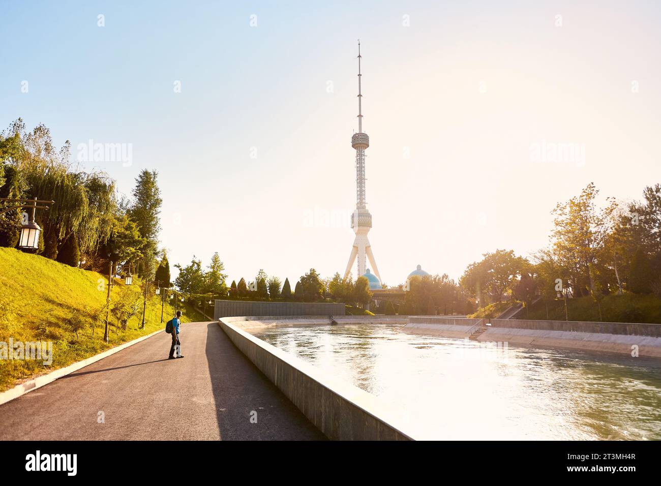 Turista con zaino che guarda la Tashkent TV Tower vicino al fiume nel parco al tramonto in Uzbekistan Foto Stock