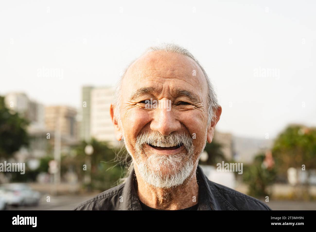 Uomo anziano felice sorridente davanti alla macchina fotografica in città - concetto di stile di vita degli anziani Foto Stock