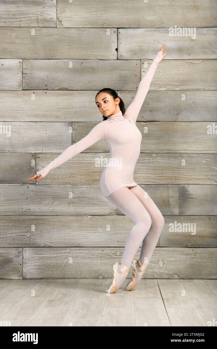 Giovane ragazza adolescente a corpo pieno con scarpe pointe che esegue una posa di balletto in piedi su uno sfondo di legno Foto Stock