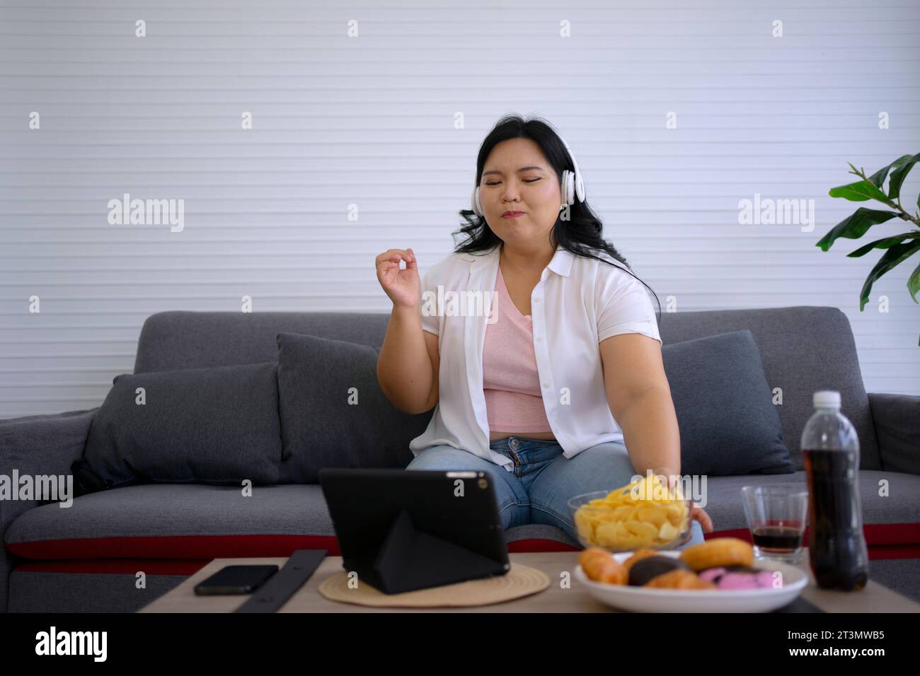 La donna Plus size sta mangiando la ciambella. Concetto di assistenza sanitaria e stile di vita. Foto Stock