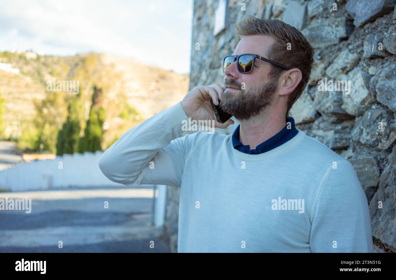 Uomo con smartphone - giovane uomo d'affari che parla con uno smartphone. Uomo d'affari professionista urbano informale che usa il cellulare e sorride una bella passeggiata. Foto Stock