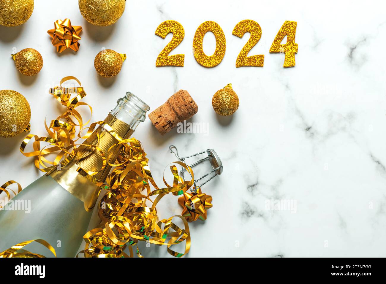 Buon anno 2024. Bottiglia di champagne con palline di natale e numeri d'oro con il numero 2024 sul tavolo di marmo. Festeggiamenti per la vigilia di Capodanno Foto Stock