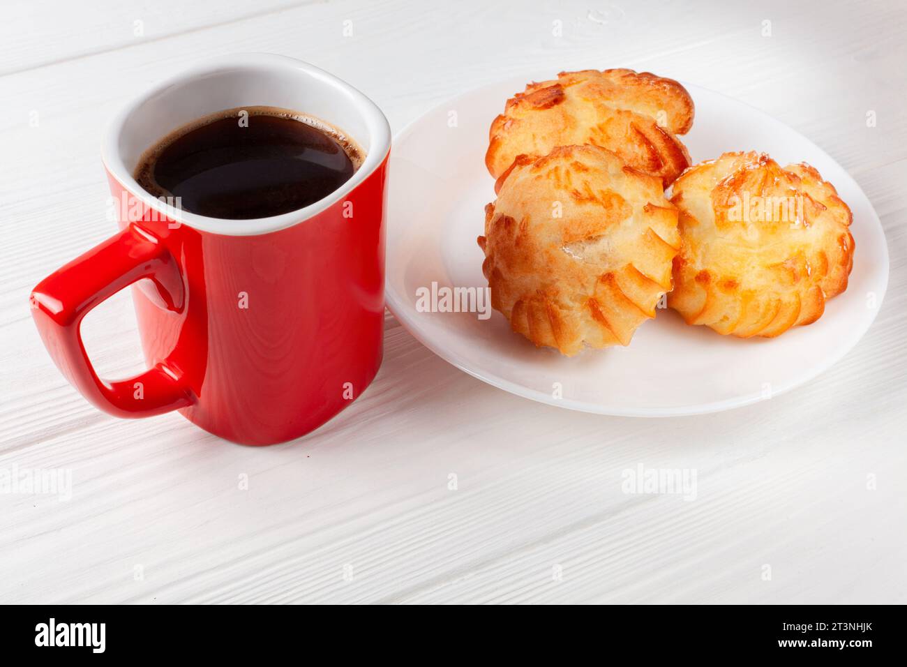 Profiterole dorate ripiene di panna, servite con una tazza di caffè su un tavolo bianco. un delizioso abbinamento di dessert per ogni occasione. Foto Stock