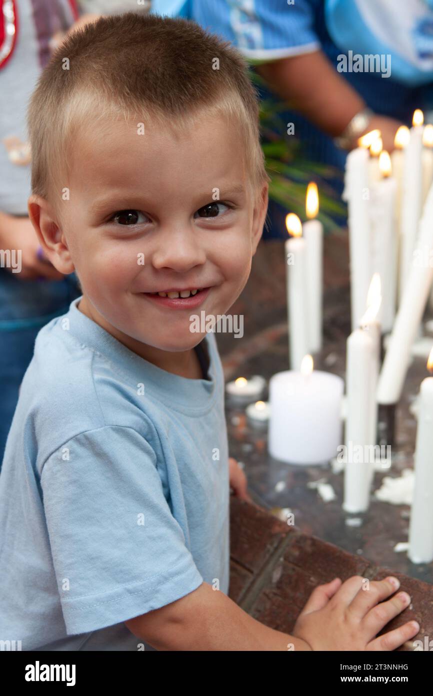 bambino sorridente con una faccia candida davanti alle candele, domenica in chiesa Foto Stock