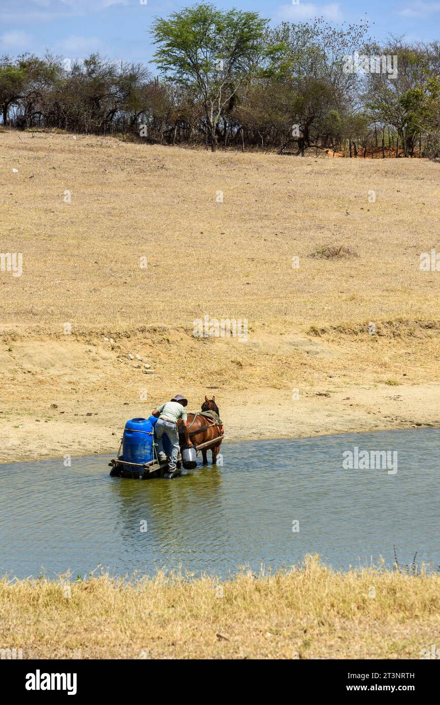 Uomo che raccoglie acqua con il cavallo in un bacino idrico a causa della siccità nelle terre di Paraiba, in Brasile, il 15 ottobre 2023. Foto Stock