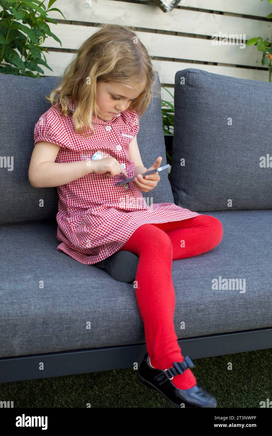 Una studentessa inglese di 5 anni seduta e che usa un telefono cellulare. Foto Stock