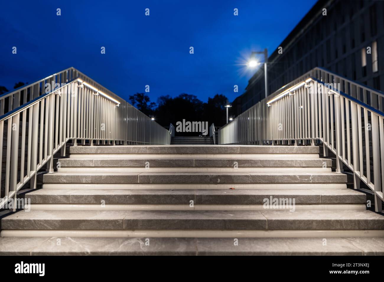 Scala esterna in pietra grigia di notte con ringhiere cromate con illuminazione incorporata. La messa a fuoco è isolata sul battistrada e sul montante della scala superiore. Foto Stock