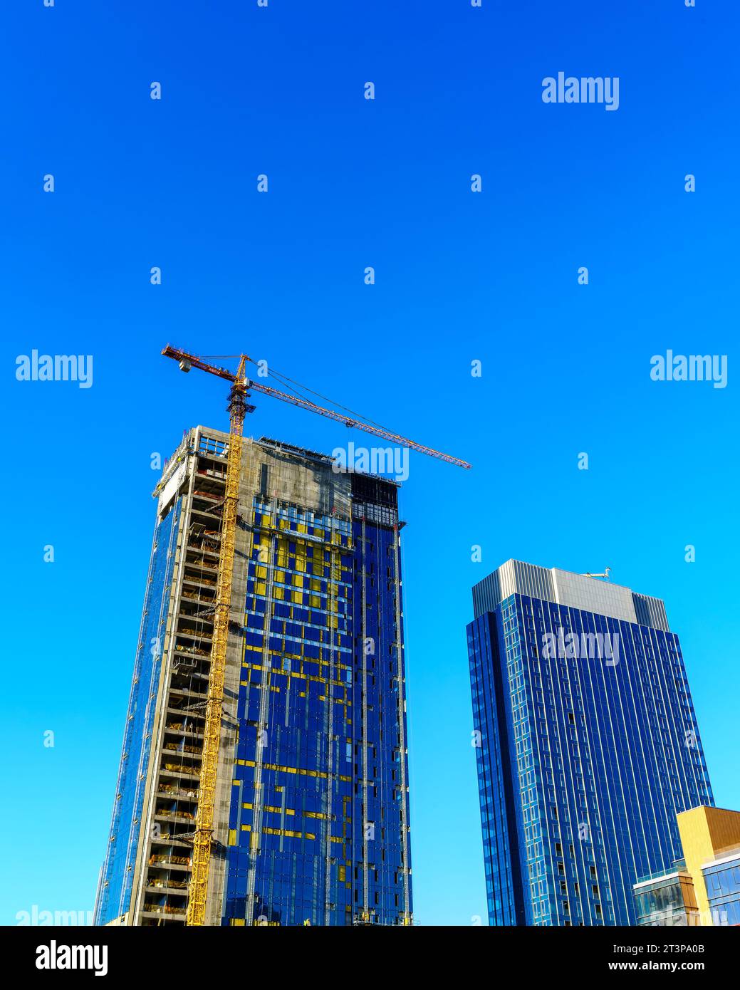 Una gru che costruisce un moderno grattacielo contro un cielo blu. Cantiere. Foto Stock