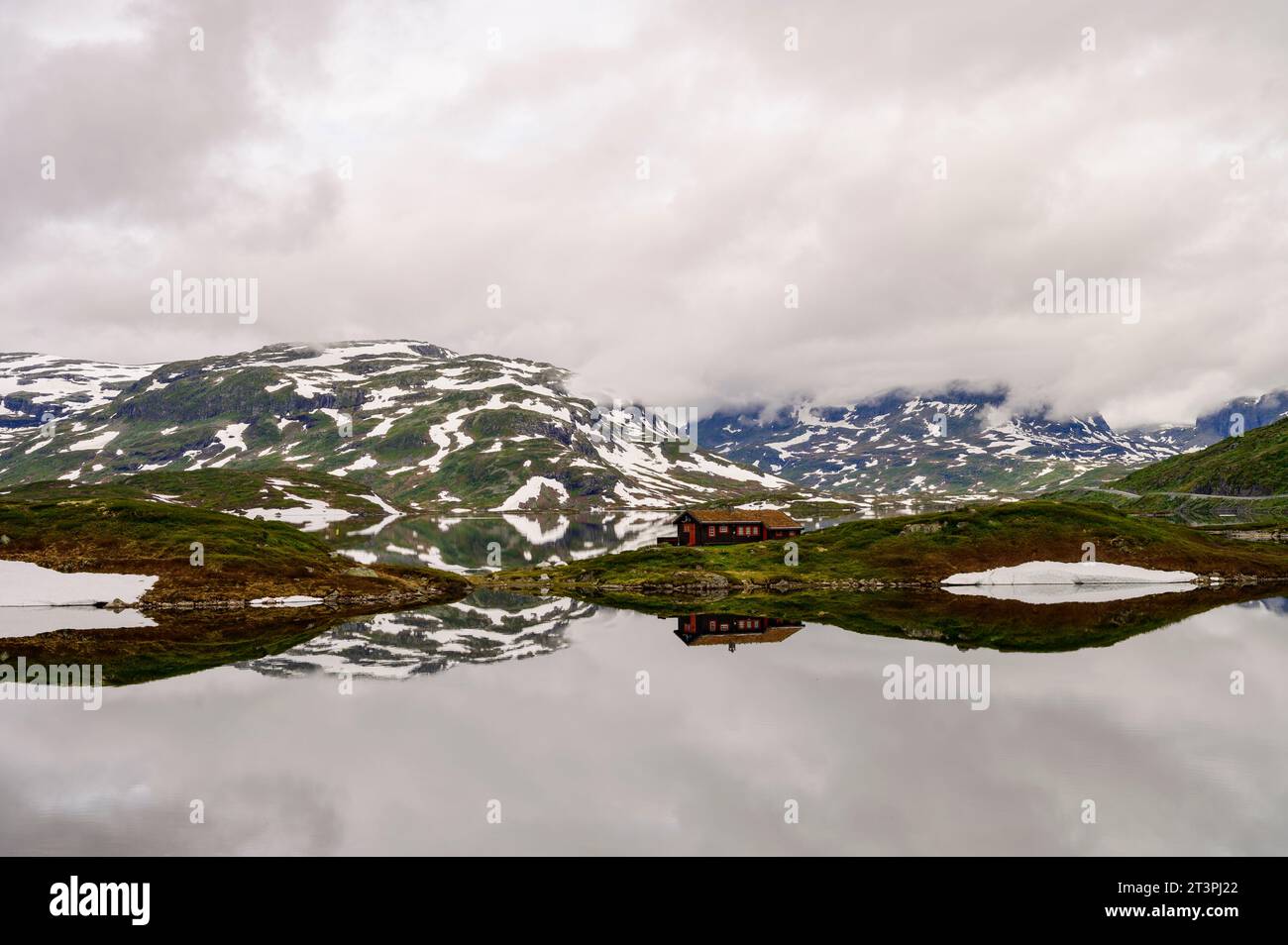 Montagne con neve e cabina solitaria che si riflettono in un tranquillo lago di Haukelifjell in Norvegia Foto Stock