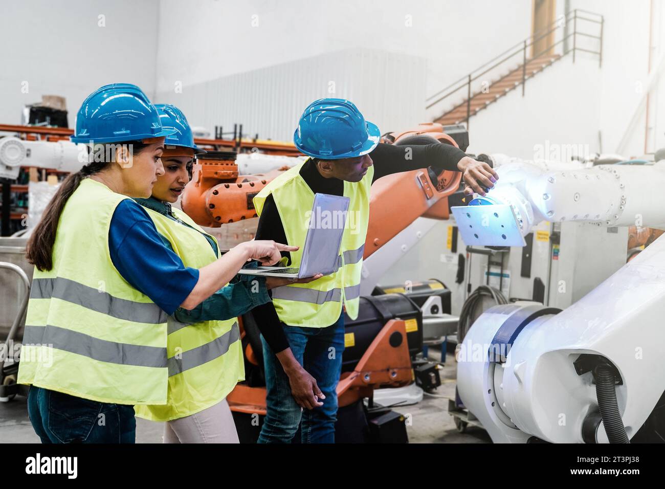 Ingegneri multirazziali che lavorano con il braccio robotizzato presso un magazzino robotizzato - persone e attività di intelligenza artificiale industriale Foto Stock