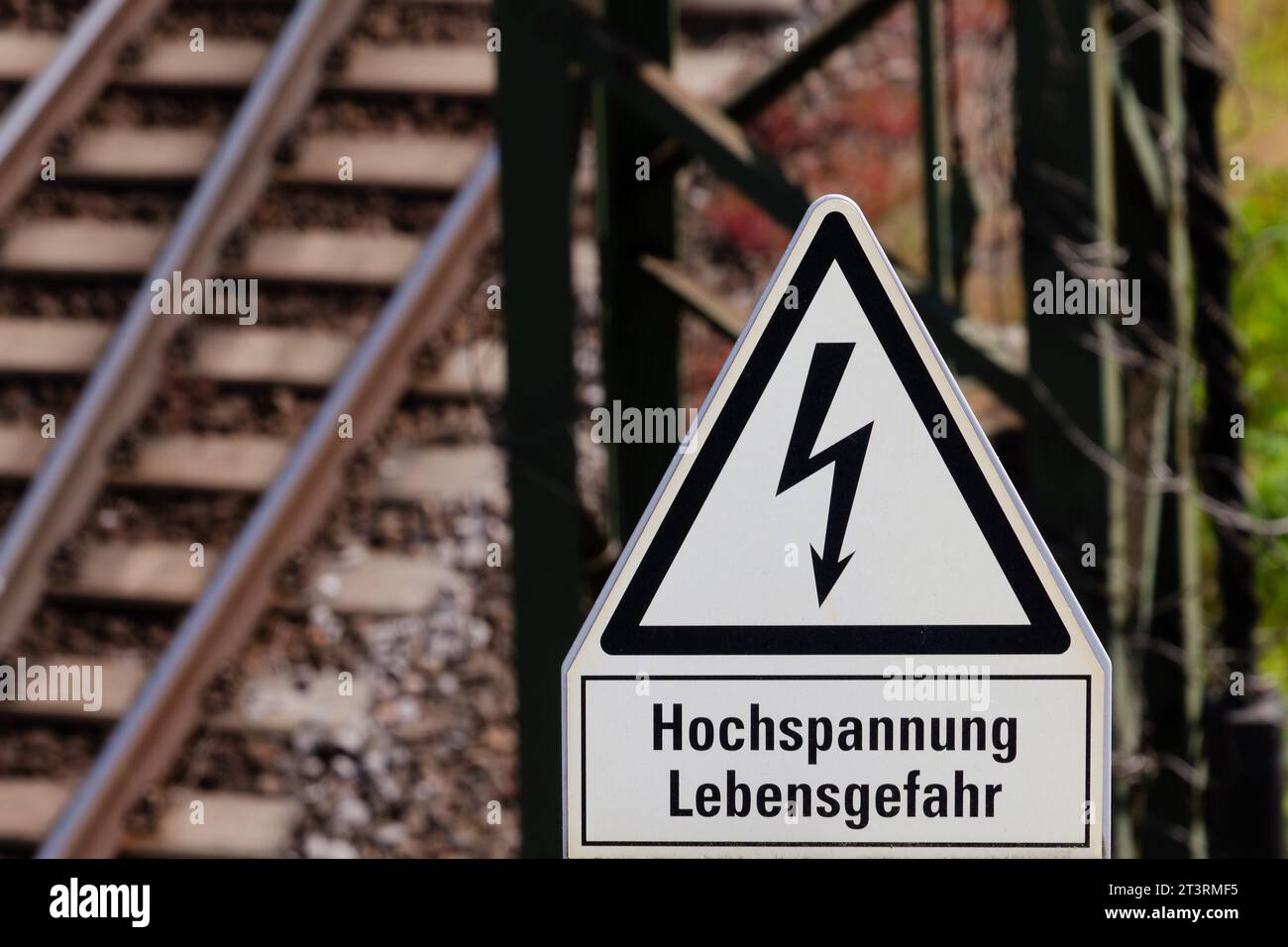 Cartello ferroviario: Alta tensione. Pericolo per la vita - in tedesco. Binari e traverse sulla sinistra. Asta di contatto in metallo sulla destra. Foto Stock
