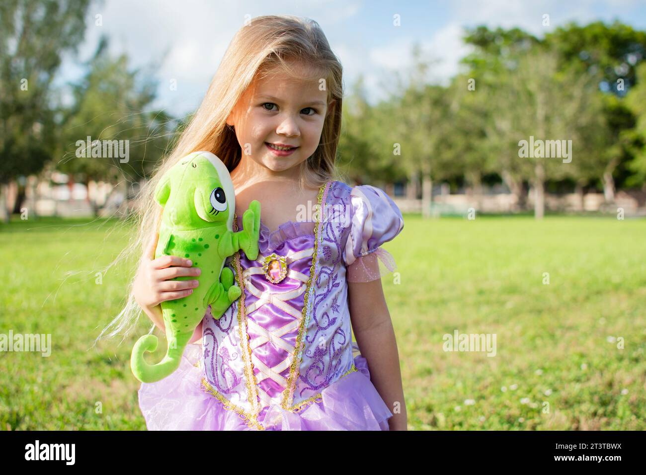 Bambina bionda dai capelli lunghi che cosplendono Rapunzel con un camaleonte Pascal. Bambina bionda con un vestito viola. Costume di Halloween, festa Foto Stock