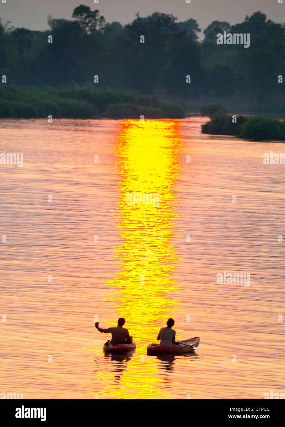 Sagome di due figure umane in kayak, che attraversano le calme e tranquille acque del Mekong, attraverso raggi di luce dorata riflessa sull'acqua, Foto Stock