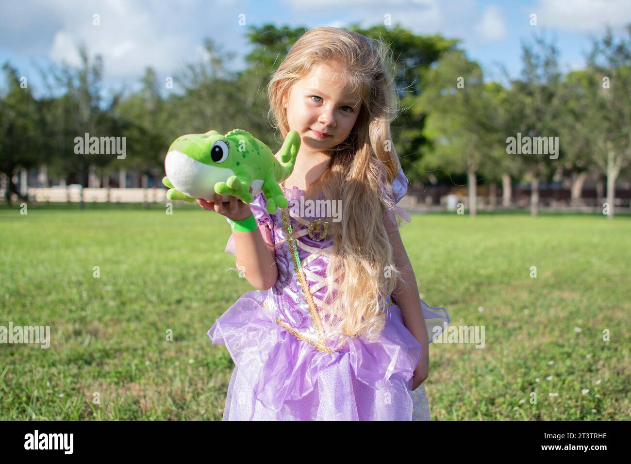Bambina bionda dai capelli lunghi che cosplendono Rapunzel con un camaleonte Pascal. Bambina bionda con un vestito viola. Costume di Halloween, festa Foto Stock