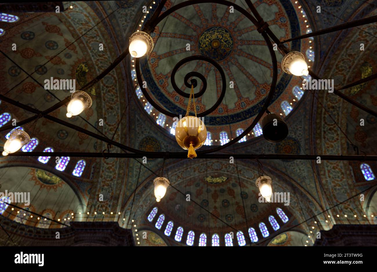 Intricate lampade e decorazioni dettagliate mettono in risalto gli interni della Moschea Blu, il tutto adagiato sul vivace soffitto a mosaico come sfondo. Foto Stock