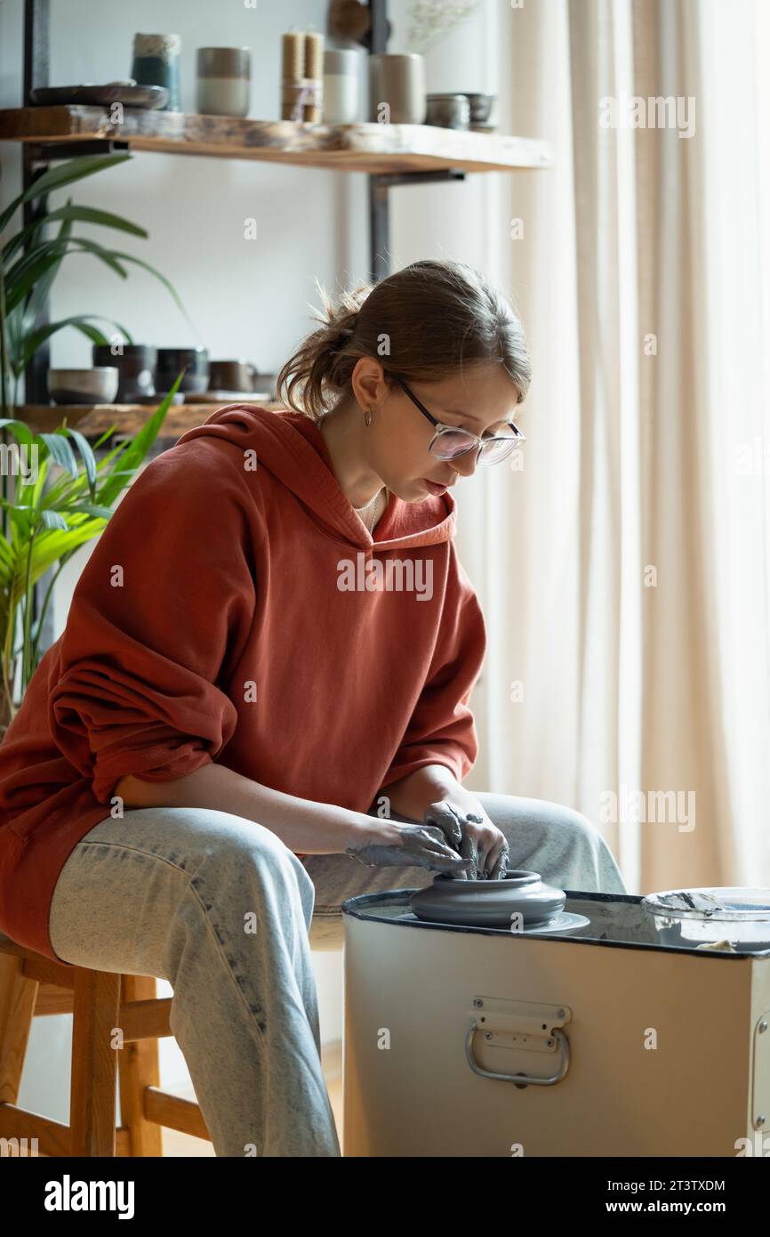 Donna rilassata che prepara utensili in argilla naturale siede in officina a un tavolo con supporto girevole Foto Stock