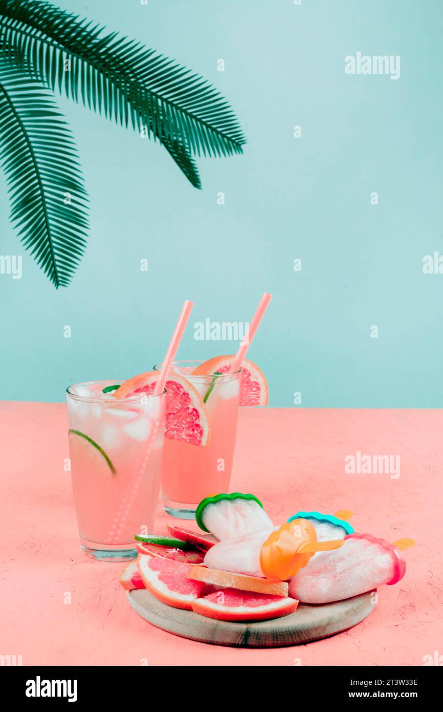 Foglie di palma bicchieri da cocktail di pompelmo ghiaccioli scrivania corallina su sfondo color tè Foto Stock