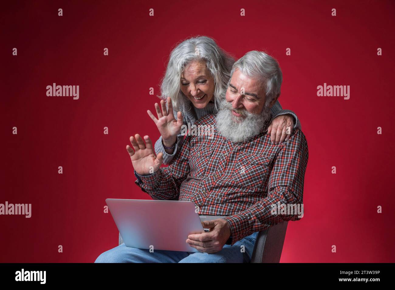 Coppia anziana che guarda un notebook che salta le mani su uno sfondo rosso Foto Stock