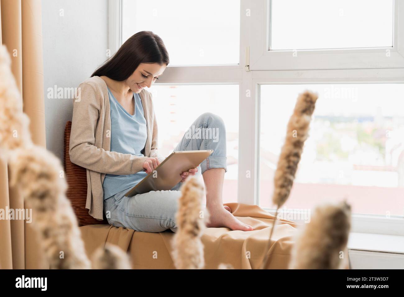 Donna con vista laterale seduta con finestra, tablet funzionante Foto Stock