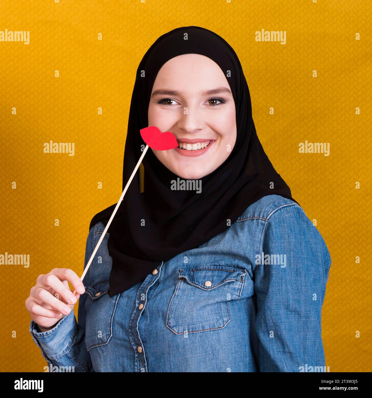 Donna musulmana sorridente che regge labbra rosse a forma di supporto di carta sullo sfondo Foto Stock