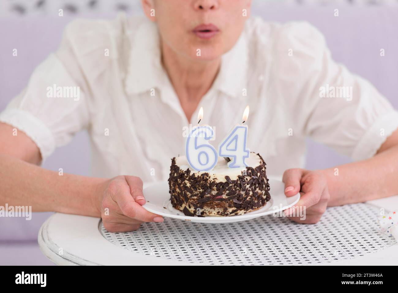 La donna che soffia il numero di candele le fa il suo tavolo da torta di compleanno Foto Stock