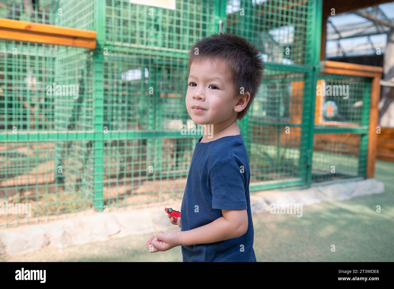 Adorabile bambino multirazziale in piedi di fronte alla gabbia con gli animali in uno zoo. Divertimento all'aperto per i bambini. Weekend in famiglia, concetto di amicizia Foto Stock
