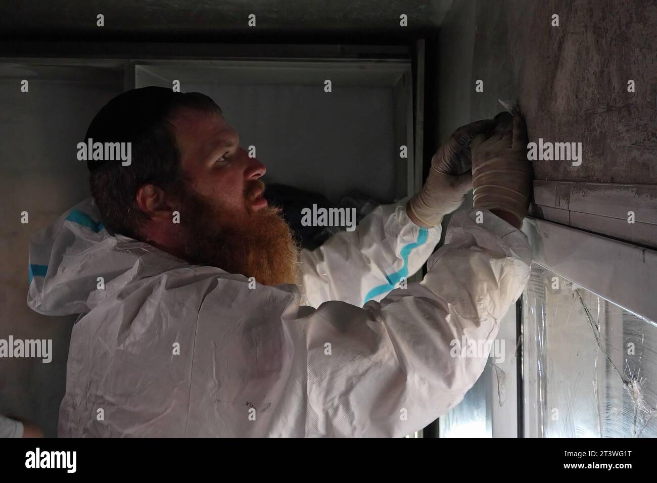 Un membro del team di identificazione delle vittime di catastrofi di Zaka Haredi lavora per pulire i resti delle vittime in modo che possano essere sepolti in conformità con la legge religiosa ebraica nel luogo in cui hanno sparato all'interno di una casa durante l'attacco del 7 ottobre da parte di militanti palestinesi di Hamas a Kibbutz Holit vicino il confine con Gaza il 26 ottobre 2023 a Holit, Israele Foto Stock