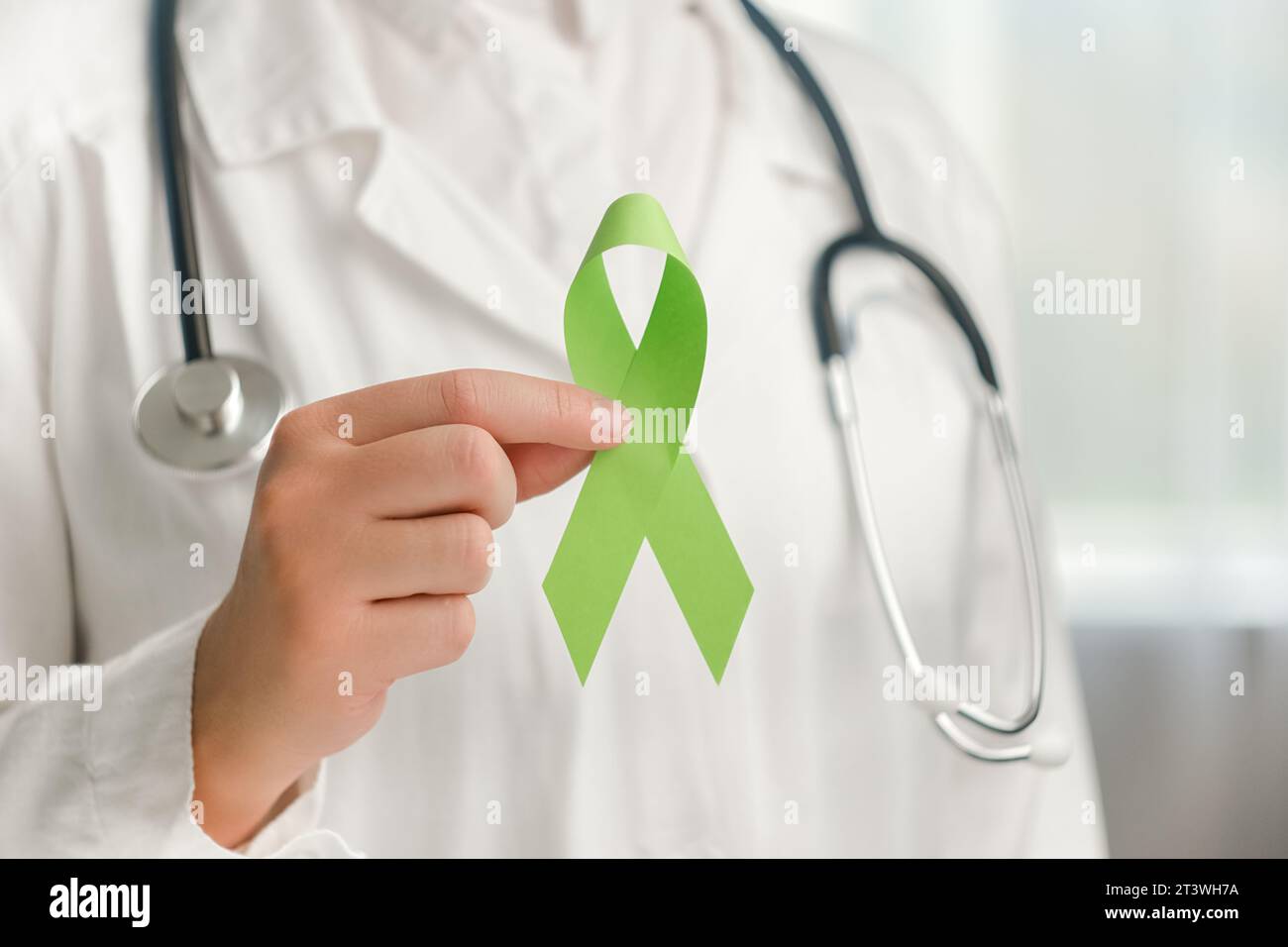 Primo piano di una giovane medico in uniforme bianca e stetoscopio con un piccolo nastro verde. Giornata mondiale bipolare. Giornata di sensibilizzazione alla salute mentale, depressione Foto Stock